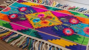 Traditional Mexican textile featuring colorful geometric patterns and embroidered floral motifs on handwoven fabric